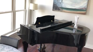 A black grand piano in a room with a large window, a painting of a beach scene, and a lamp.
