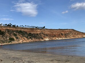 A coastal landscape with a sandy beach, a rocky cliff, and a calm sea. - Beautiful apartment 2ch 2sdb Las Ramblas Golf Orihuela (villacosta)