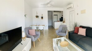 A living room with a TV, two armchairs, a sofa, a dining table, and a kitchen in the background. - Beautiful apartment 2ch 2sdb Las Ramblas Golf Orihuela (villacosta)