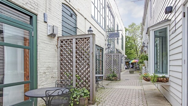 A narrow alleyway with a table and chairs, a wooden lattice partition, and a building with a sign reading 'BELLAVITA.'