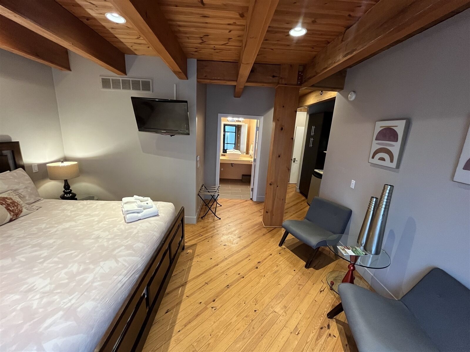 Habitación de hotel con cama, televisión, silla y mesa con lámpara.