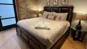 A bedroom with a bed, a nightstand, a lamp, a wall with three framed pictures, and a window.