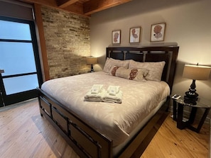 A bedroom with a bed, a nightstand, a lamp, a wall with three framed pictures, and a window.