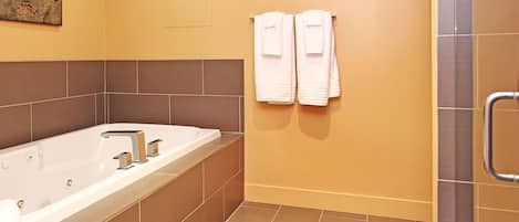A modern bathroom with a large bathtub, a shower area, and two towels hanging on the wall.