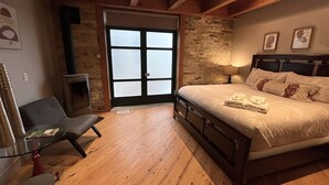 A bedroom with a large bed, a chair, a fireplace, and a stone wall.
