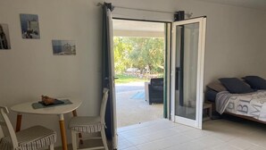 Ein Zimmer mit Esstisch und Stühlen, einem Bett mit gemustertem Überwurf und einer Schiebeglastür, die zu einem Außenbereich führt.