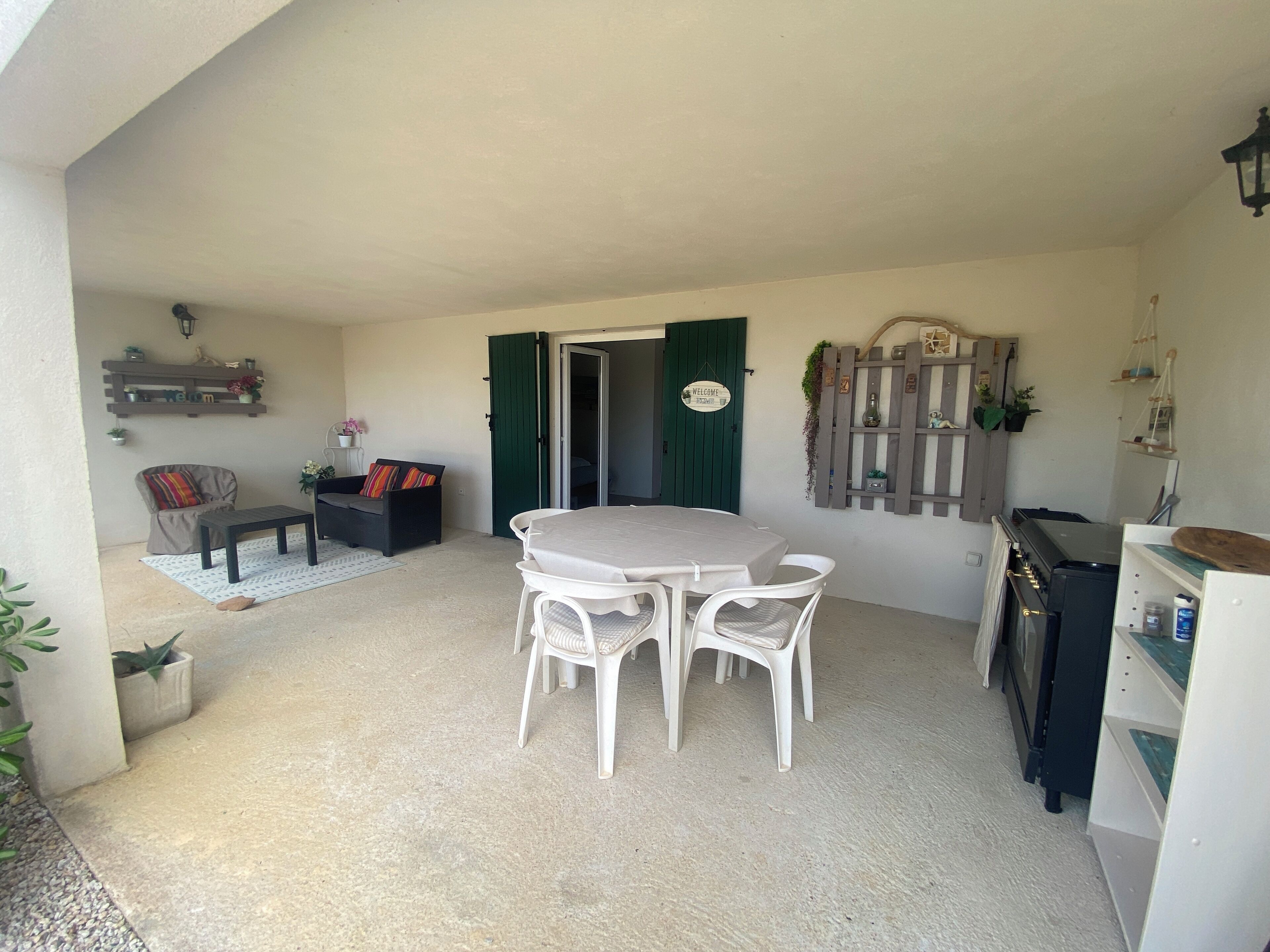 A covered patio area with a round table and four chairs, a sofa, a small table, and a cabinet with a stove.
