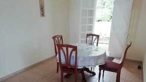 Zona de menjador amb una taula rodona i quatre cadires, una porta blanca i un sòl amb rajoles.