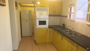 Una cuina compacta amb armaris grocs, un refrigerador blanc, una placa de cocció i un rentaplat.