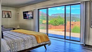 A bedroom with a bed, a TV, and a large sliding glass door leading to an outdoor area with a view of mountains. - Uptown Sedona, Prime Location, HotTub VIEWS (Sedona)