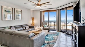 Una sala de estar moderna con un sofá seccional grande, un ventilador de techo y vistas a la playa a través de amplios ventanales correderas.