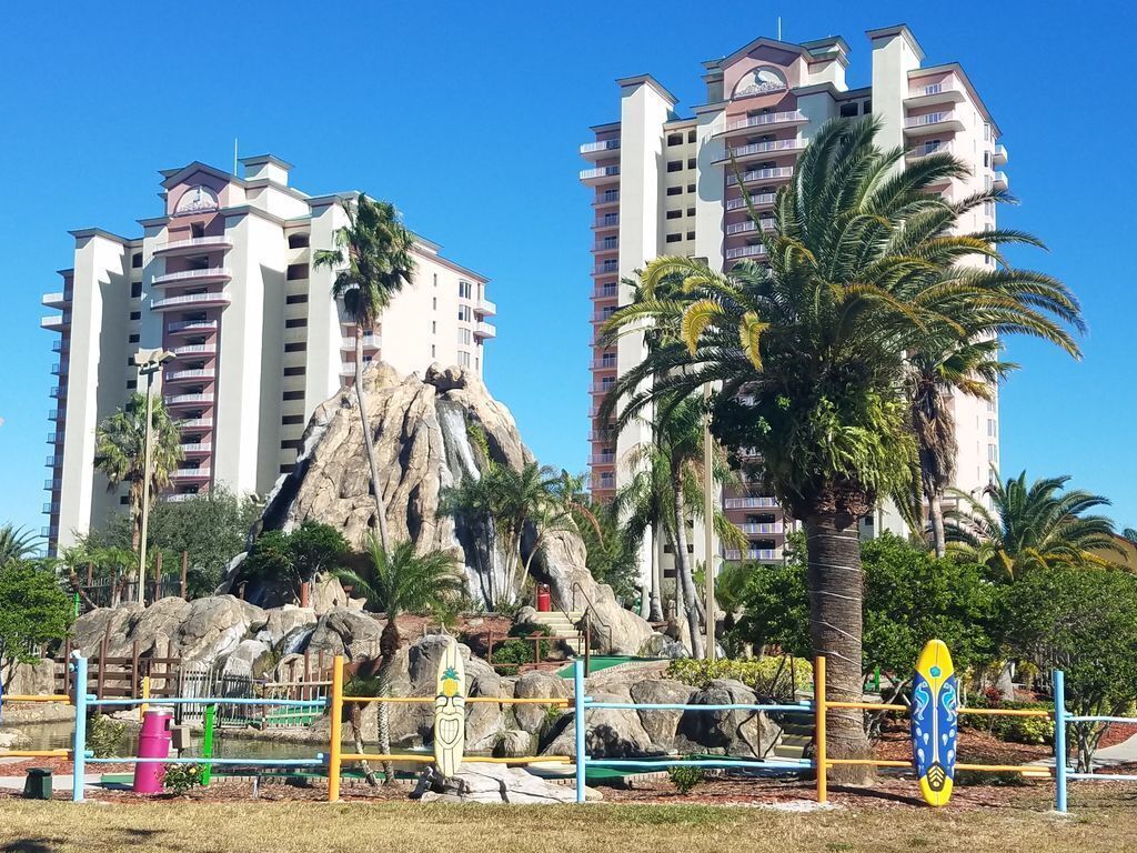 Um hotel com vários andares, uma formação rochosa e palmeiras.