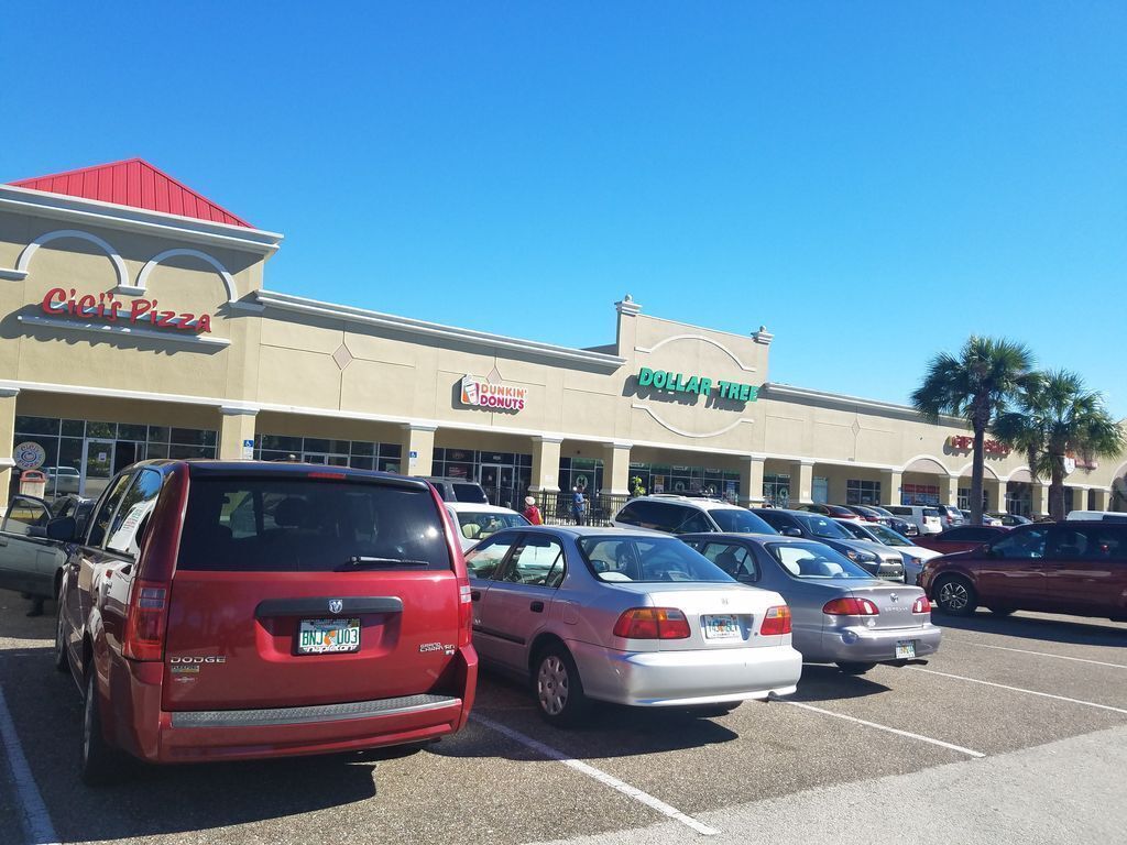 Un estacionamiento con varios autos estacionados frente a un edificio con varios letreros de negocios, incluyendo 'Cici's Pizza' y 'Dunkin' Donuts'.