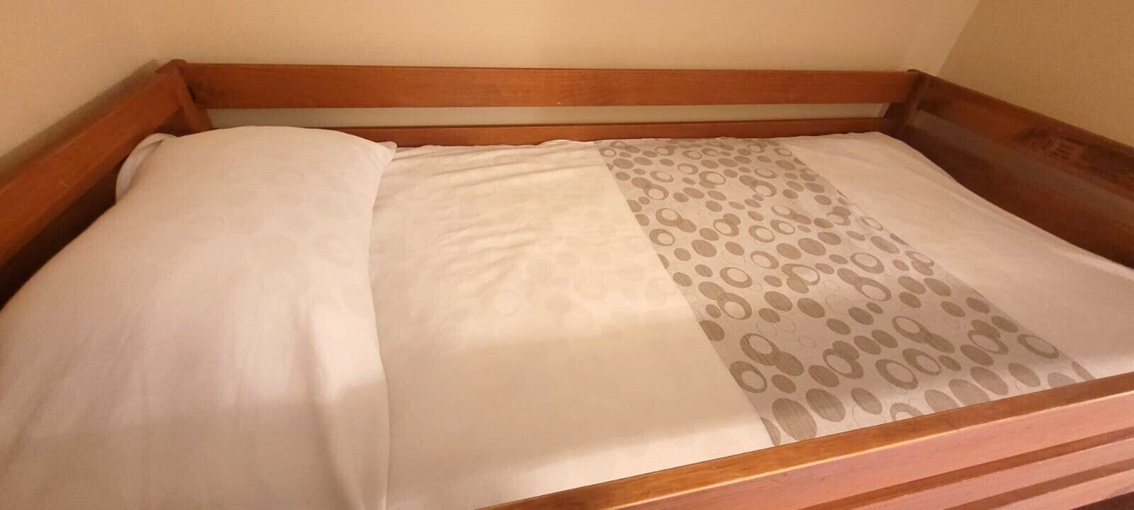 A wooden bed with a white mattress and a patterned pillow.