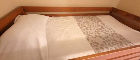 A wooden bed with a white mattress and a patterned pillow.