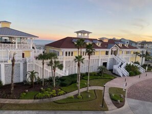 Stunning coastal hotel with connected buildings, balconies, and a covered walkway, set amidst lush greenery and palm trees.