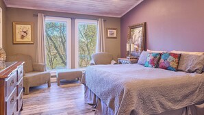 Une chambre à coucher avec un grand lit, une chaise, une commode et une fenêtre donnant sur des arbres.