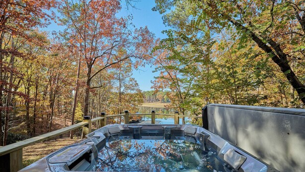 Un bain à remous situé dans une zone boisée, avec une terrasse en bois et une vue sur un lac en arrière-plan.