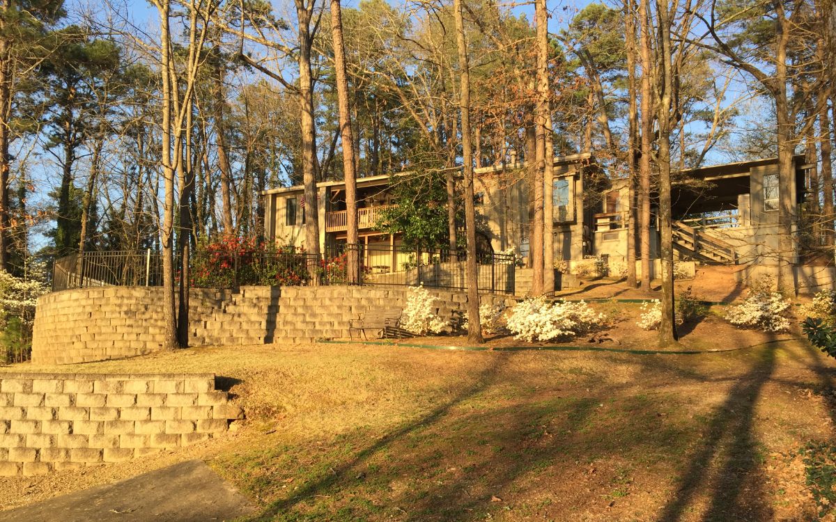 A rustic cabin with a stone foundation, wooden beams, and a balcony overlooking a forested area.