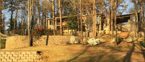 A rustic cabin with a stone foundation, wooden beams, and a balcony overlooking a forested area.