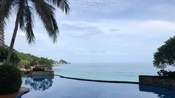 A clear view of a swimming pool with a curved edge, a palm tree, and a distant view of the sea and a small island. - Beautiful Condo in Playas Gemelas, Puerto Vallarta (Puerto Vallarta)
