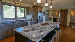 A modern kitchen with marble countertops, stainless steel appliances, and pendant lighting.