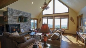 A spacious living room with a stone fireplace, leather sofas, and large windows offering a view of the outdoors.