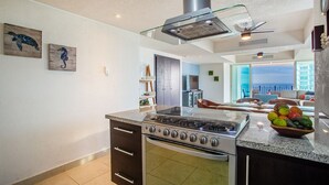 A modern kitchen with a gas stove, oven, and a glass range hood. There is a dining area with a view of the ocean. - OCEANFRONT CONDO IN TROPICAL PARADISE AWAITS YOU AT THE GRAND VENETIAN! (Las Glorias)