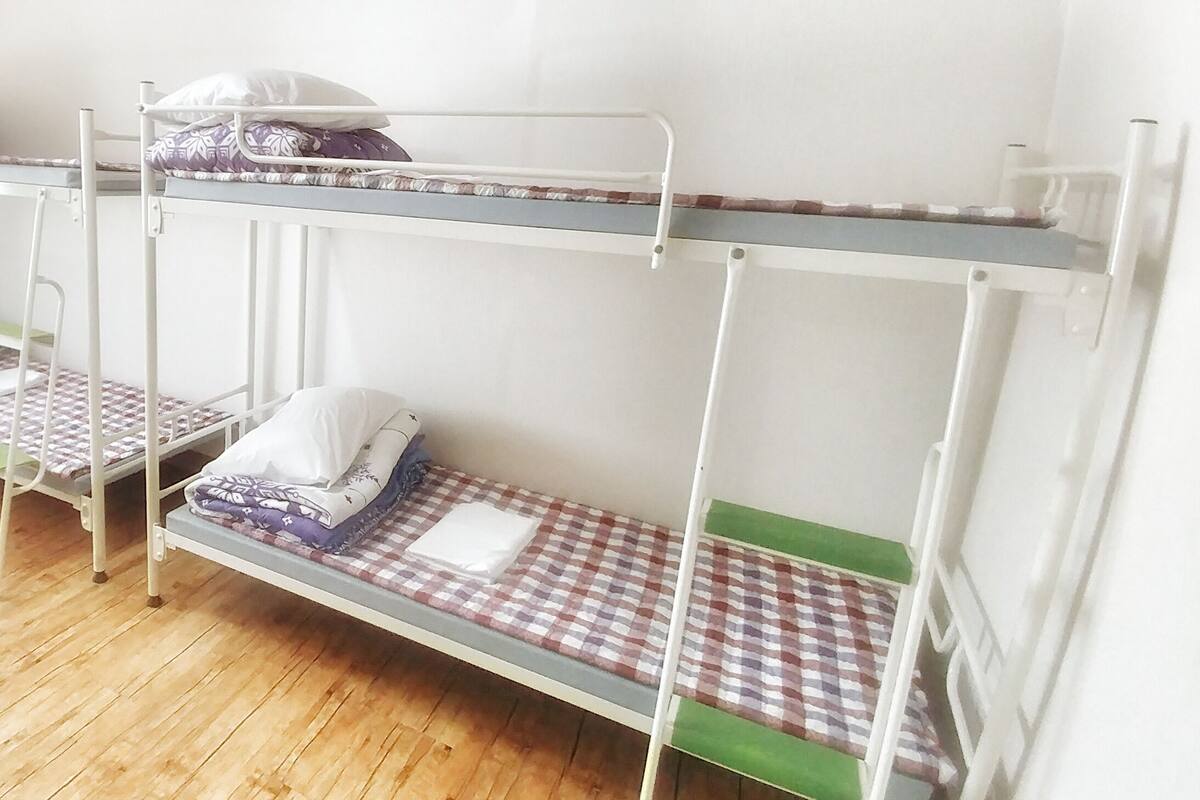 Une chambre de dortoir avec des lits superposés, un plancher en bois et un mur blanc uni.