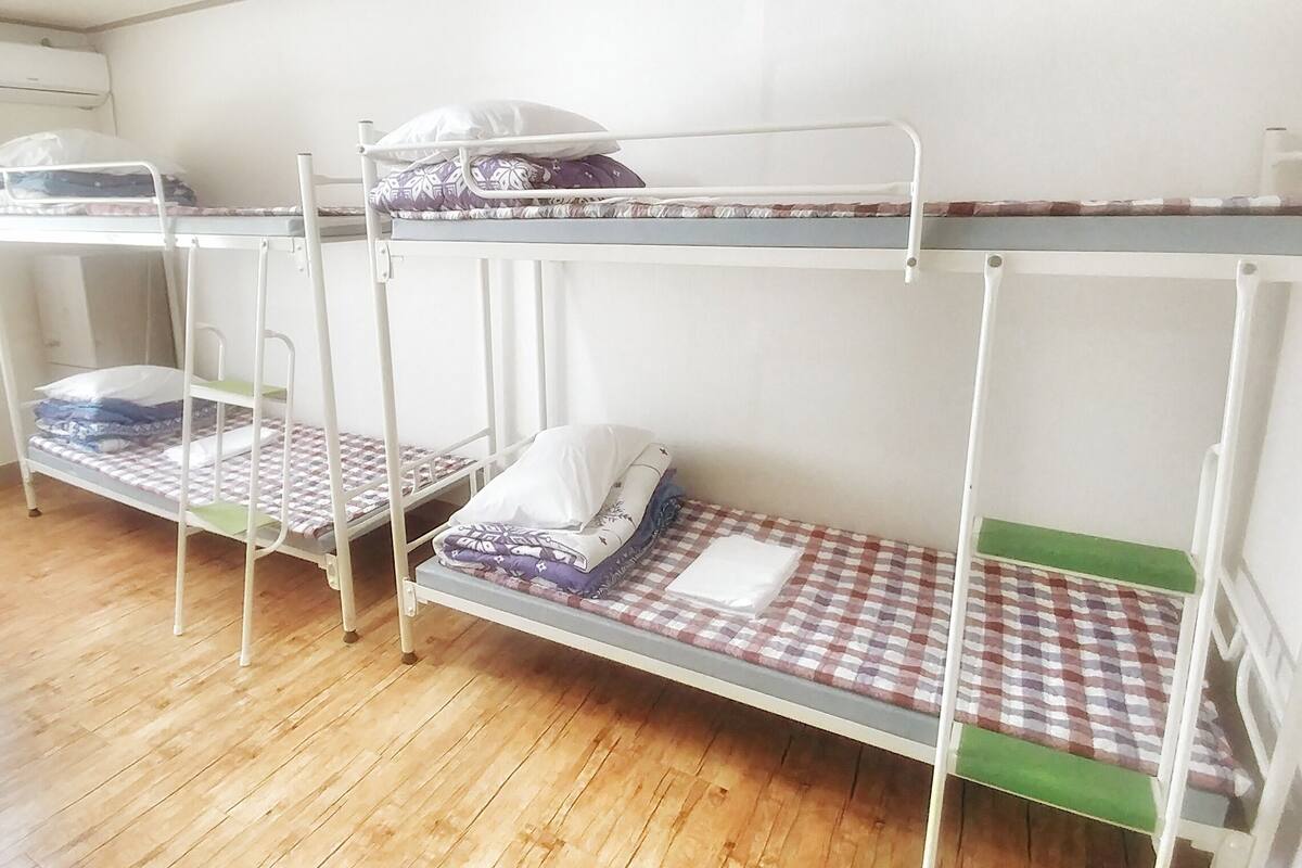 Une pièce avec trois lits superposés, un plancher en bois et un mur blanc.