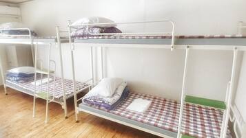 A room with three bunk beds, wooden flooring, and a white wall.