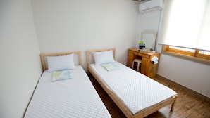 Une chambre avec deux lits simples, un bureau en bois, un miroir et un appareil de climatisation.