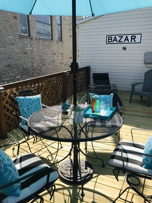 An outdoor patio with a round metal table, blue patterned chairs, and a 'BAZAR' sign on a white building. - Walk to Downtown - 10 Mins to Starved Rock! (Lasalle)