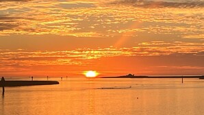 A sunset over a calm body of water with a distant shoreline and a few structures.