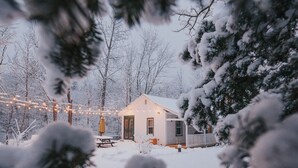 Una cabana petita coberta de neu, amb terrassa de fusta i llums encadenades.