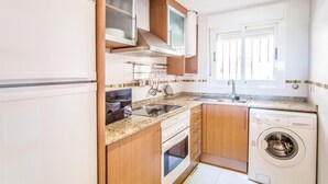 A compact kitchen with a built-in oven, a washing machine, and a window with blinds.