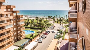 A multi-story hotel with a pool, beach view, and parking area.