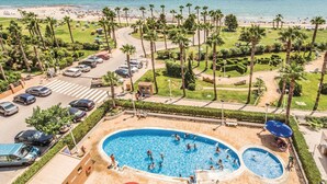 A pool area with multiple swimming pools, surrounded by palm trees and a view of the beach.