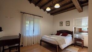 A bedroom with a wooden bed, a bedside table, a desk, and a window with curtains.