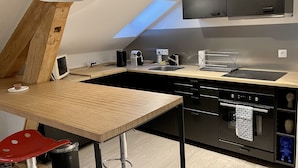 A modern kitchen with a wooden ceiling, a skylight, a black countertop, a sink, a coffee maker, and a dishwasher.