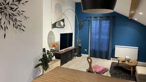A modern living room with a TV, wooden furniture, a hanging lamp, and a blue accent wall.