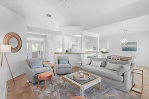 Een ruime woonkamer met een grijze bank, twee fauteuils, een salontafel en een eethoek met een houten tafel en stoelen.