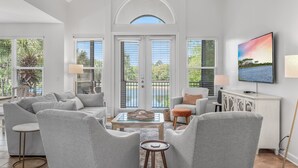 A spacious living room with a high ceiling, large windows, and a view of the outdoors. - Pet Friendly ~ Community Pool (Miramar Beach)