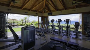 Ett gym med olika träningsredskap, en bänk och utsikt över havet och palmerna.