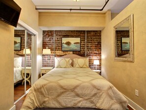 A bedroom with a brick-patterned headboard, a large bed with patterned bedding, bedside lamps, and a mirror on the wall. - Heated Pool Access | 5*Clean | Flex Cancelation (Savannah)