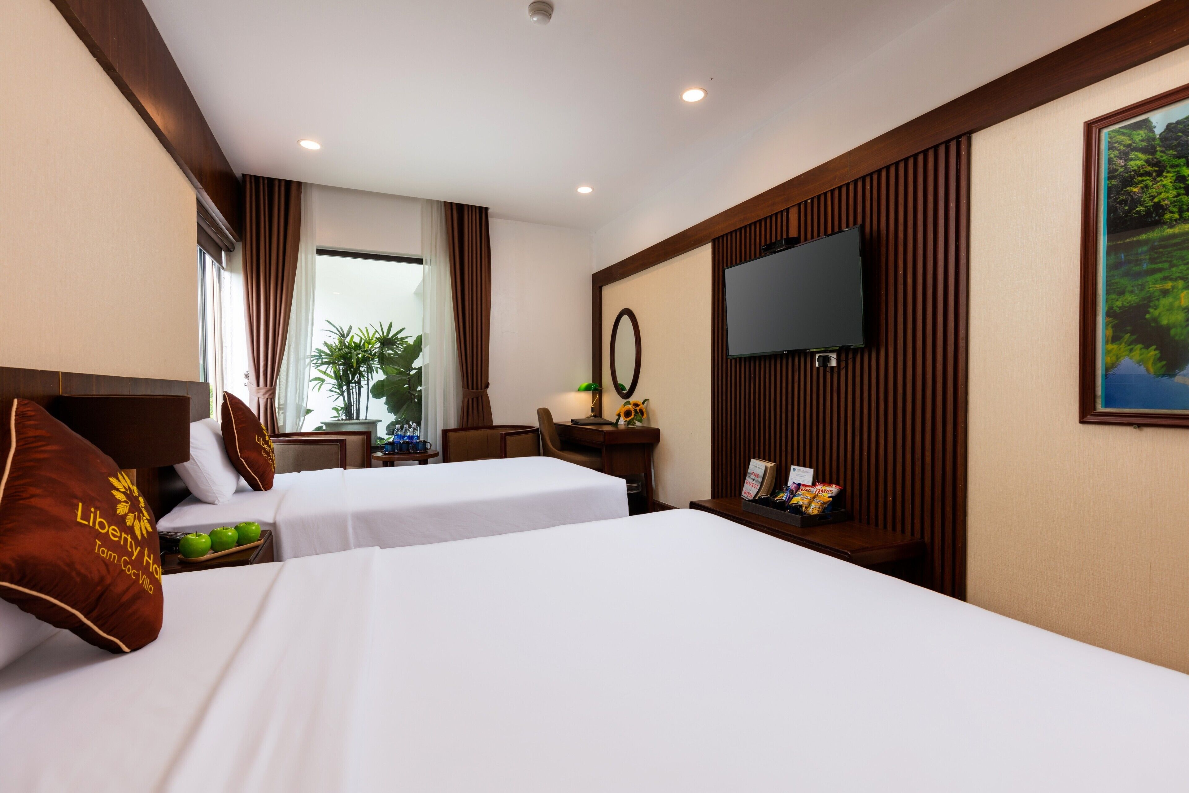A hotel room with two beds, a TV, a desk, and a window with curtains.