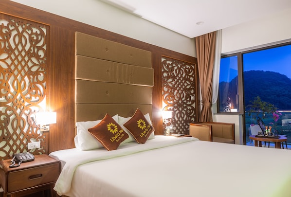 Habitación de hotel con una cama grande, dos lámparas de noche, una mesita con un teléfono y vistas a un paisaje montañoso a través de un ventanal amplio.