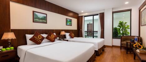 A hotel room with two beds, a desk, a chair, a lamp, and a window with a view of greenery.