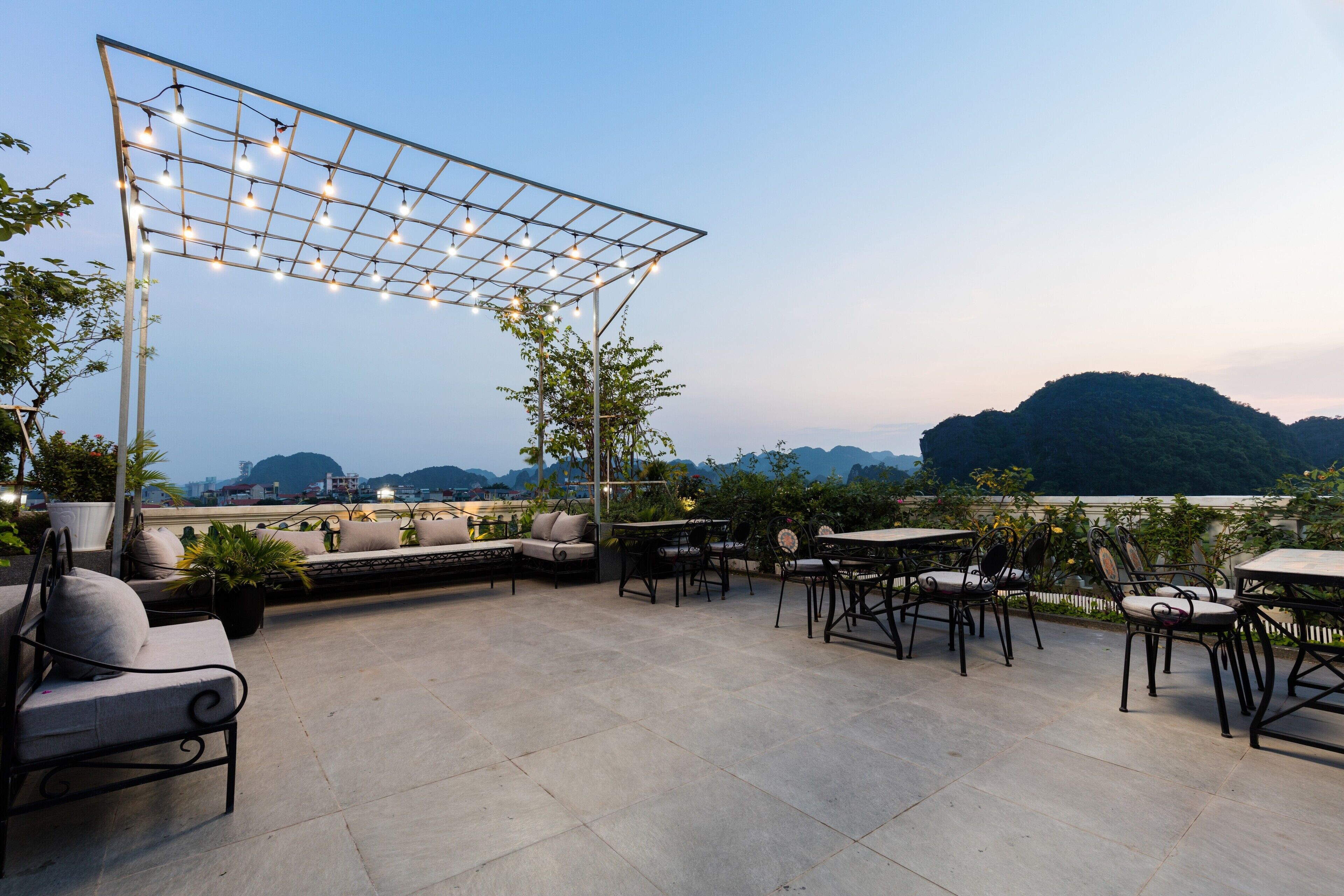 Un patio al aire libre con arreglos de asientos, una pérgola con luces colgantes y vistas a colinas distantes.