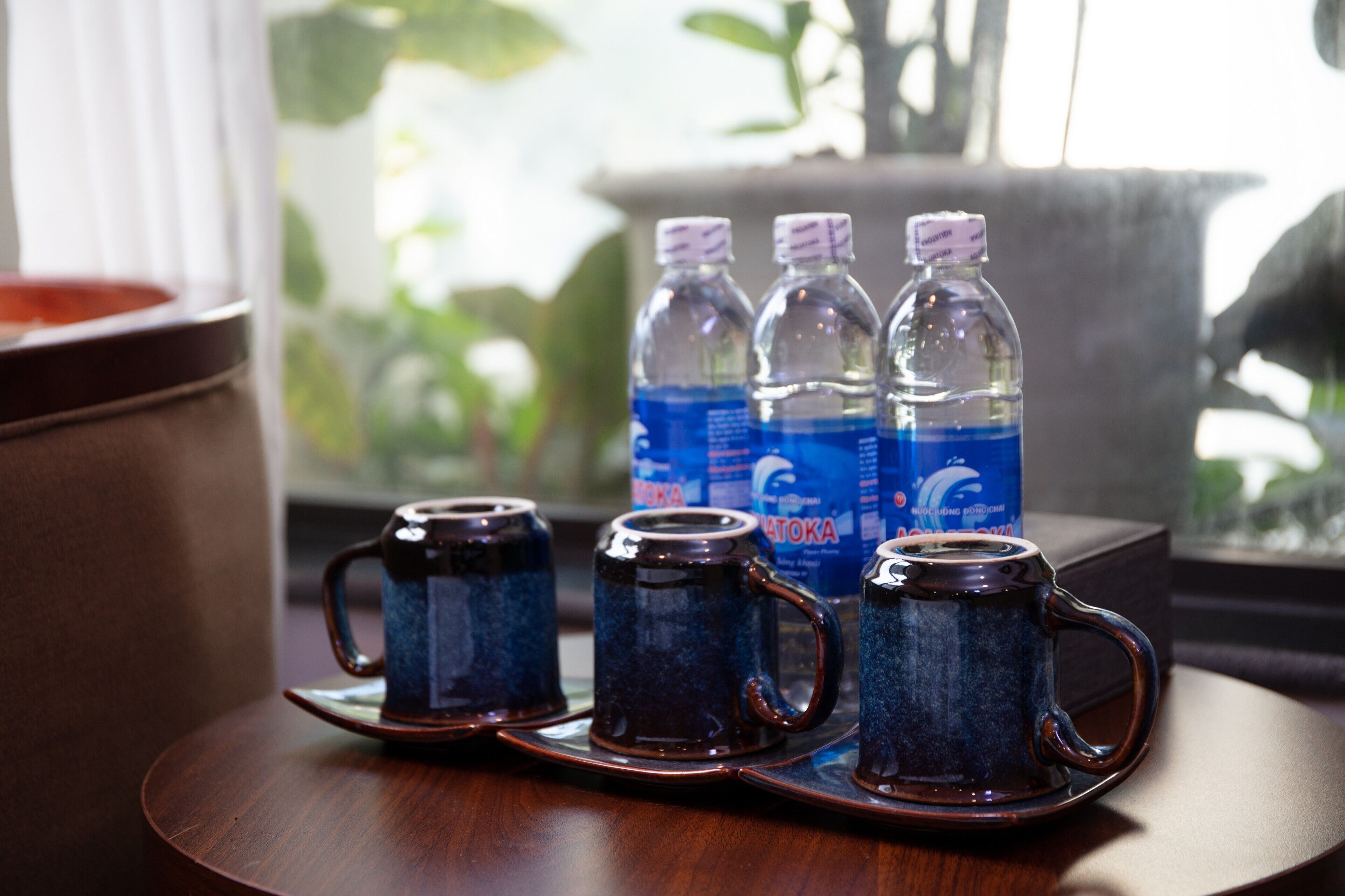 A tray with three dark blue ceramic mugs on a wooden table, with water bottles in the background.